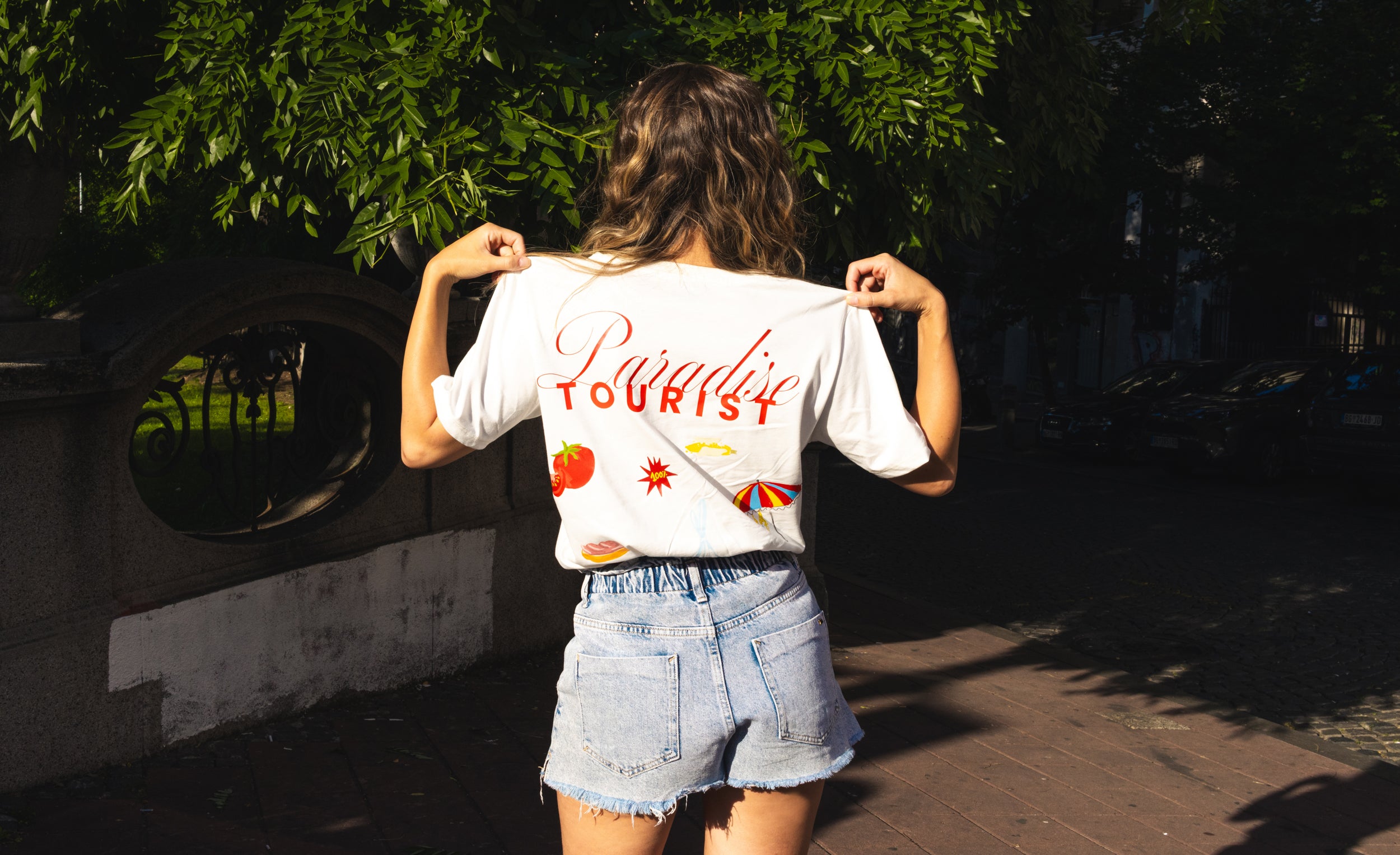 Person wearing a white t-shirt with 'Paradise Tourist' text, Ivica i Majica new collection for summer.